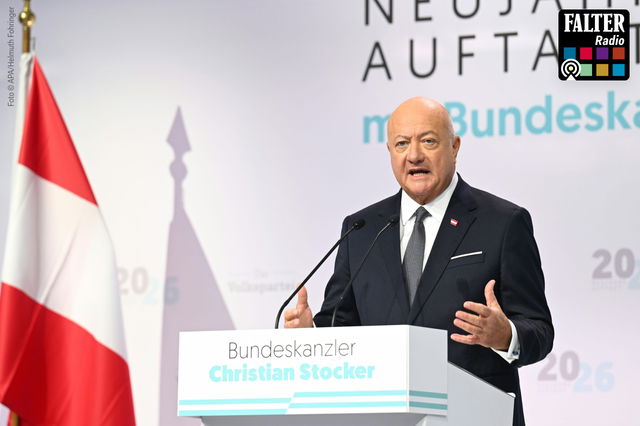(Dieser ALT-Text wurde mithilfe von KI erstellt) Ein Mann im Anzug spricht am Rednerpult mit der Aufschrift „Bundeskanzler Christian Stocker“, links eine österreichische Flagge.