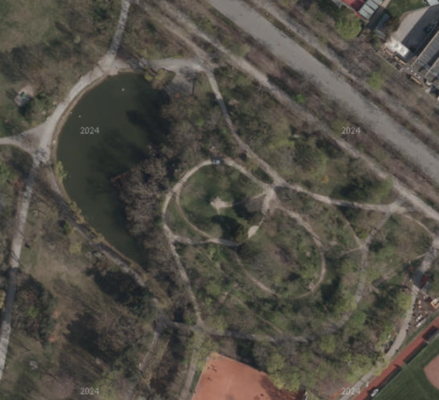 (Dieser ALT-Text wurde mithilfe von KI erstellt) Satellitenbild zeigt einen Park mit Wegen, einem Teich links oben und umliegender Vegetation aus der Vogelperspektive.