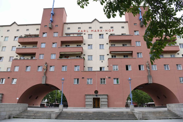 (Dieser ALT-Text wurde mithilfe von KI erstellt) Vorderansicht des Karl-Marx-Hofs in Wien mit Schriftzug, Balkonen, zwei großen Torbögen und Statuen an der Fassade.
